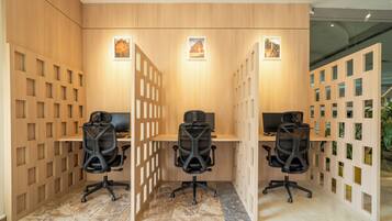 Un espace de bureau moderne comprenant trois bureaux, chacun équipé d’un fauteuil de bureau noir, et une cloison en bois avec des panneaux ajourés.