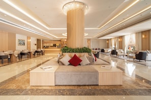 A spacious lobby with a central seating area, a reception desk, and a modern chandelier.