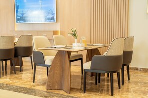 A dining area with a wooden table, six chairs, a vase with flowers, and a menu stand. - Innyar Hotel (Riyadh)