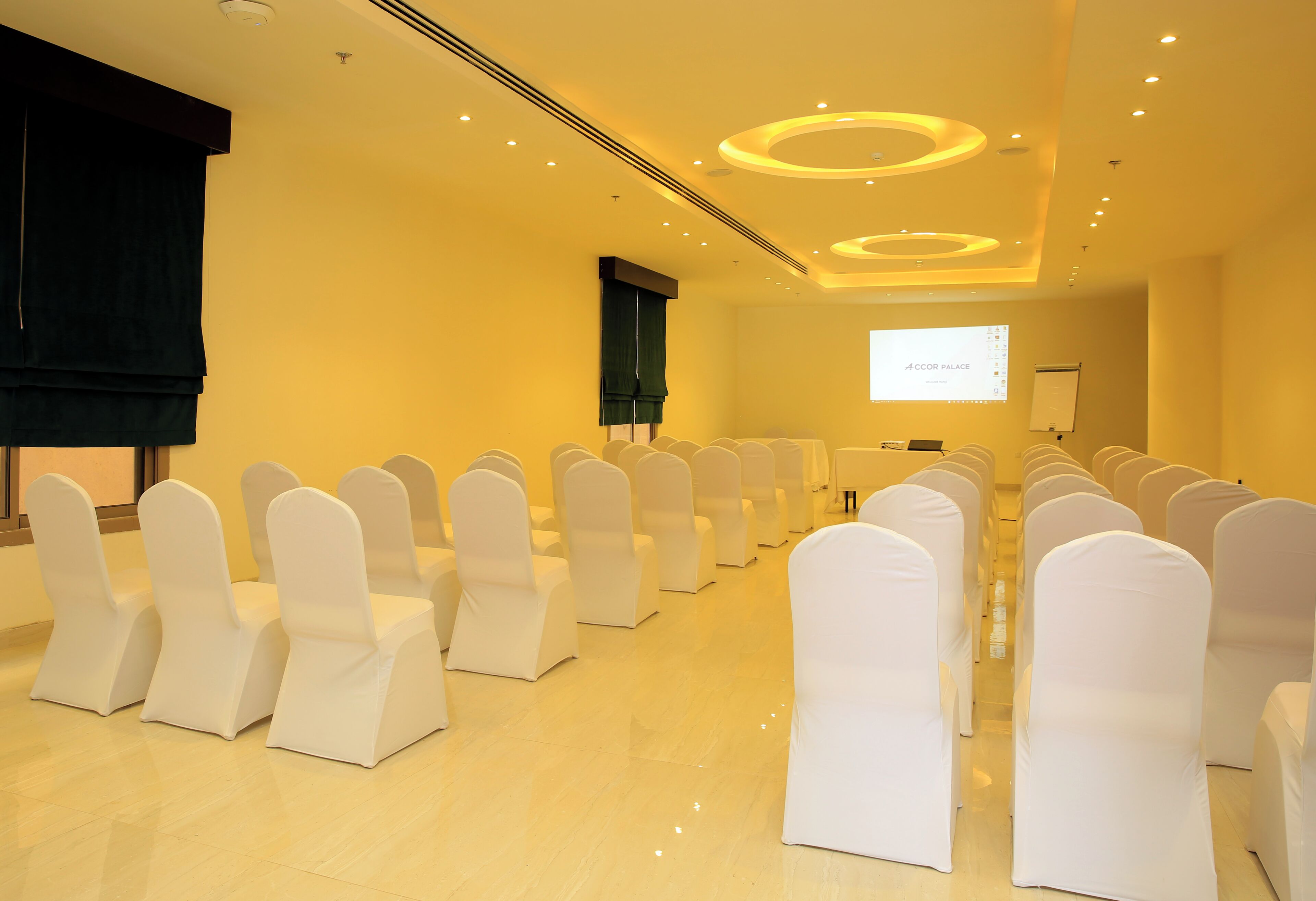 A conference room with rows of white chairs, a projector screen, and a presentation area.