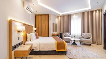 A modern hotel room with a bed, bedside tables, a desk, a chair, and a sofa.