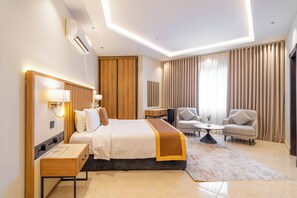 A modern hotel room with a bed, bedside tables, a desk, a chair, and a sofa.