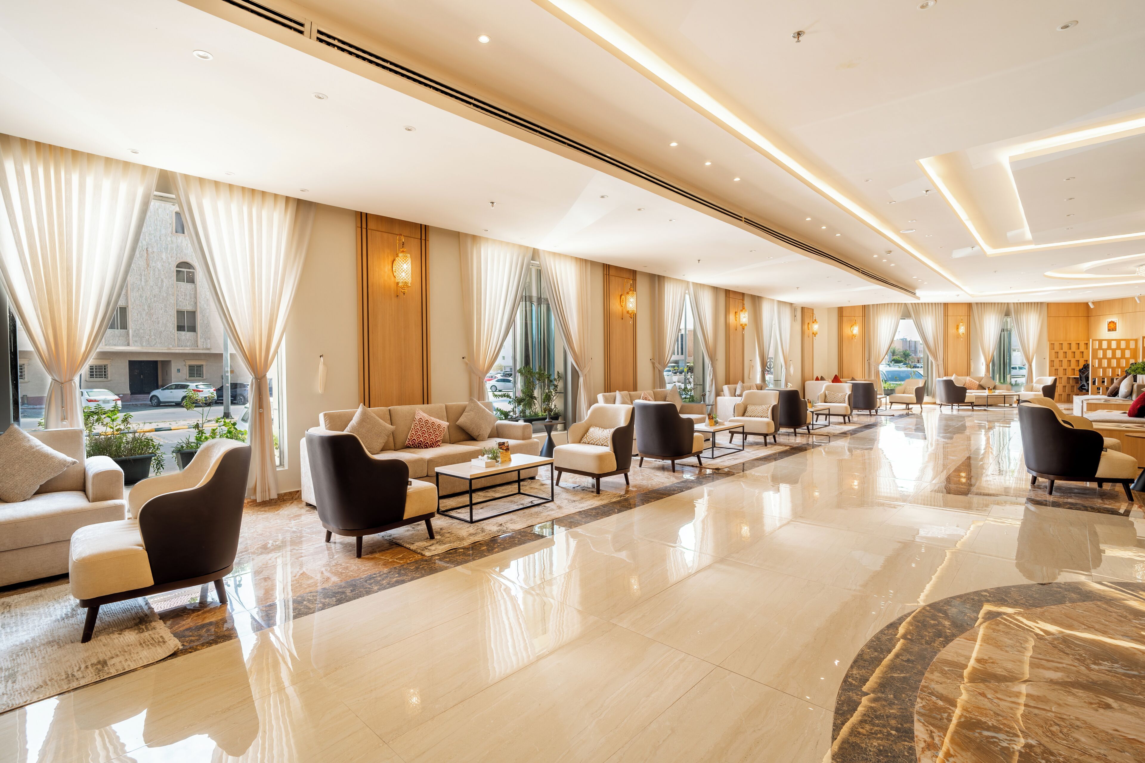 A spacious hotel lobby with a polished marble floor, multiple seating areas, and large windows offering a view of the street.