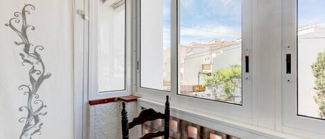 A room with a large window, a wooden chair, a dining table with a plate and cutlery, and a decorative wall design.