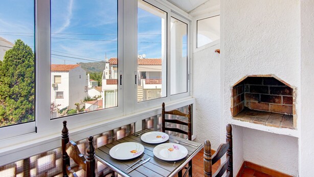 A dining area with a table set for two, a brick oven, and a view of the neighborhood through large windows. - LOS ANGELES 53 Roses (Rosas / Roses)