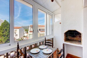A dining area with a table set for two, a brick oven, and a view of the neighborhood through large windows.