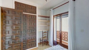 A bedroom with a bed, a wooden wardrobe, a chair, and a window with curtains. - LOS ANGELES 53 Roses (Rosas / Roses)