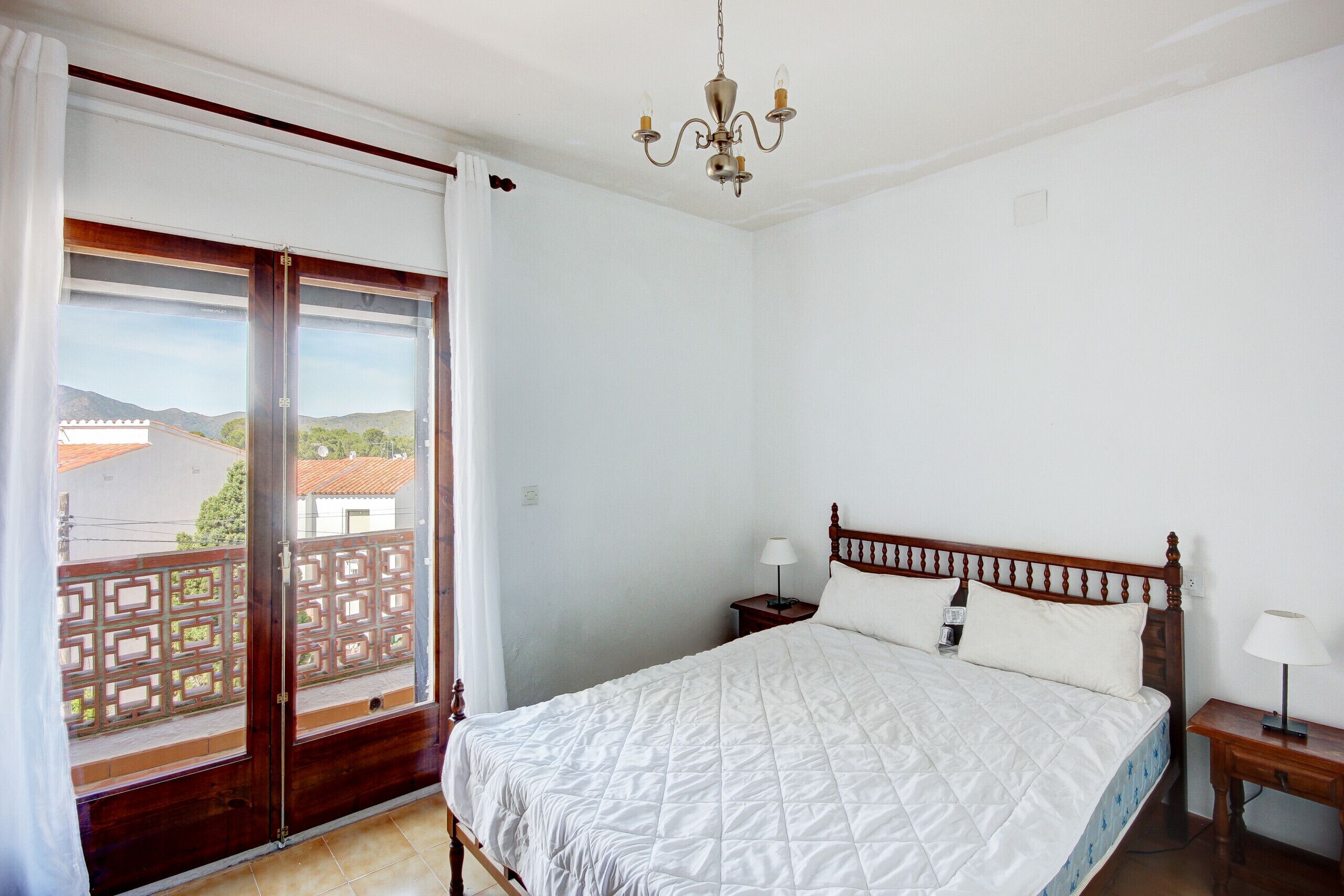 Un dormitorio con cama, mesita de noche, candelabro y puerta corrediza de cristal que da a un balcón.