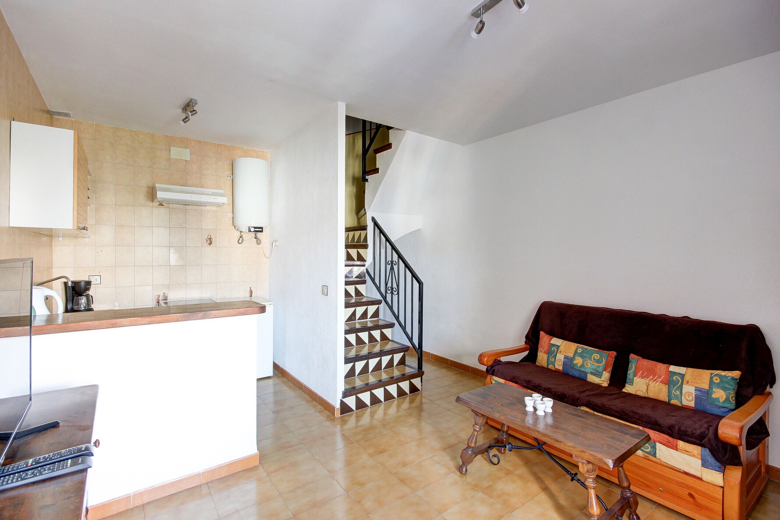 A kitchen with a stove, a coffee maker, and a sink. There is a staircase leading to a landing. A sofa and a small table are in the living area.