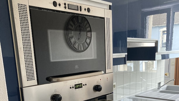 Una cocina con horno empotrado, reloj digital y pileta de acero inoxidable.