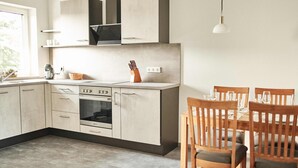 A modern kitchen with a dining area. It includes a stove, oven, and cabinets. There are chairs and a table set for dining. - Vacation apartment at the Winzerhof with a view of the vineyards. (Stadecken-Elsheim)