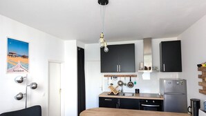 A modern kitchen with a wooden table and bar stools, black cabinets, and a stainless steel refrigerator. - Central Arcachon: Modern 2BR Apartment with Terrace, 400m from Beach (Arcachon)