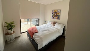 Un dormitorio con cama, ventana con persianas, planta en maceta y una obra de arte en la pared.