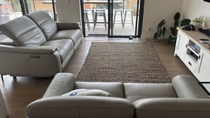 Una sala de estar moderna con un sofá color beige, un tapete estampado y vistas a la ciudad a través de amplias ventanas.