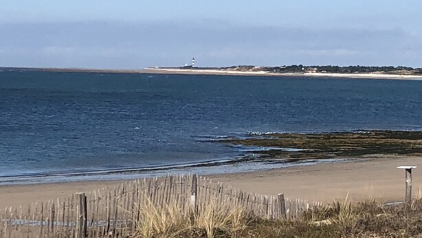 A beach with a lighthouse in the distance, a wooden fence, and a clear sky. - Charming renovated country house Chéray Oléron ( 3 stars) (saint georges d'oléron)