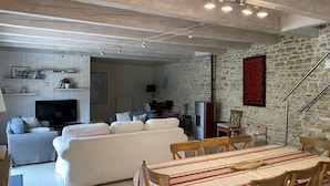 A spacious living area with a sofa set, a dining table with chairs, a television, and a stone wall. - Charming renovated country house Chéray Oléron ( 3 stars) (saint georges d'oléron)