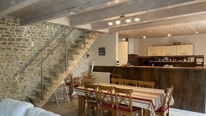 A modern kitchen with a stone wall, wooden staircase, and a dining area with a table and chairs. - Charming renovated country house Chéray Oléron ( 3 stars) (saint georges d'oléron)