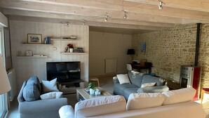 A living room with a TV, sofas, a coffee table, and a stone wall. - Charming renovated country house Chéray Oléron ( 3 stars) (saint georges d'oléron)