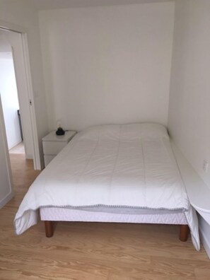 Un dormitorio con una cama individual, una mesita de noche y una puerta que da a otra habitación.