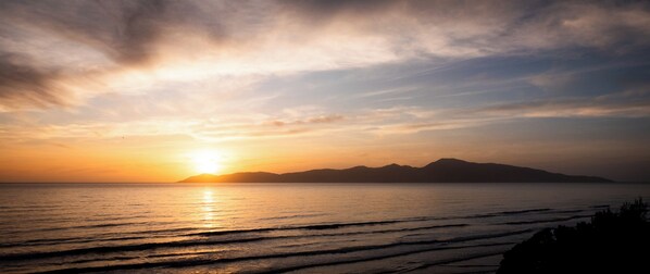 A sunset over a calm sea with distant mountains.