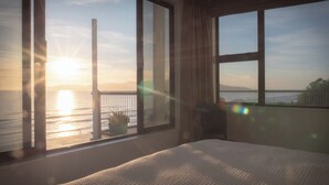 Ein Schlafzimmer mit großem Fenster mit Blick auf ein Gewässer und eine entfernte Brücke.