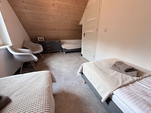 Quarto com duas camas, uma escrivaninha, uma cadeira e um guarda-roupa.