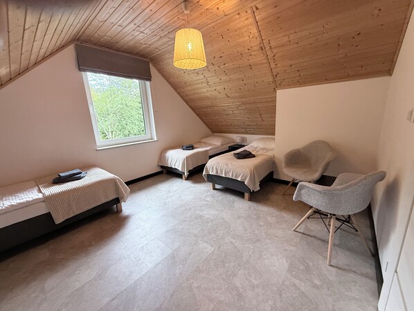 A bedroom with a sloped ceiling, two beds, a window, a chair, and a hanging light fixture.