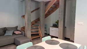 Una sala moderna con un sofá, una mesa de comedor con sillas, una escalera y un armario blanco.
