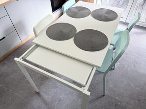 Et køkken med et hvidt bord, fire vævede bordskåner og turkise stole.