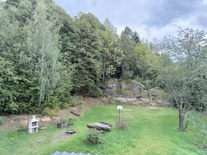 Un área exterior con césped, una estructura de piedra, mesas de picnic y una canasta de baloncesto.