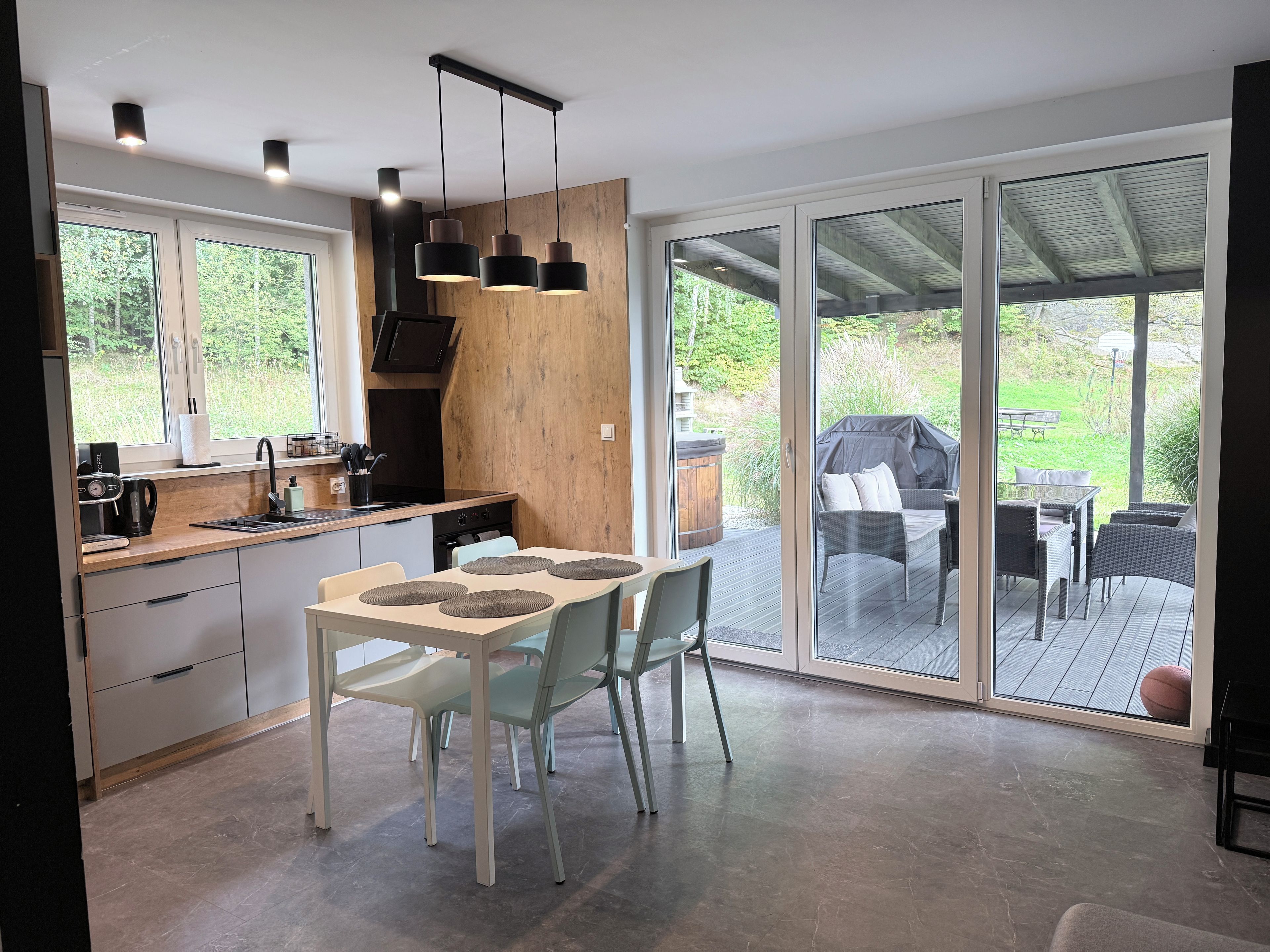 A modern kitchen with a dining area, large sliding glass doors leading to an outdoor patio with furniture.