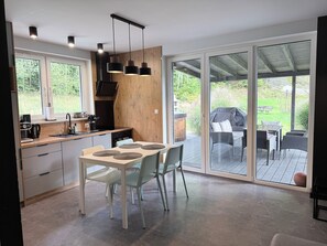 Een moderne keuken met een eetgedeelte, grote schuifdeuren die uitkomen op een terras buiten met meubilair.