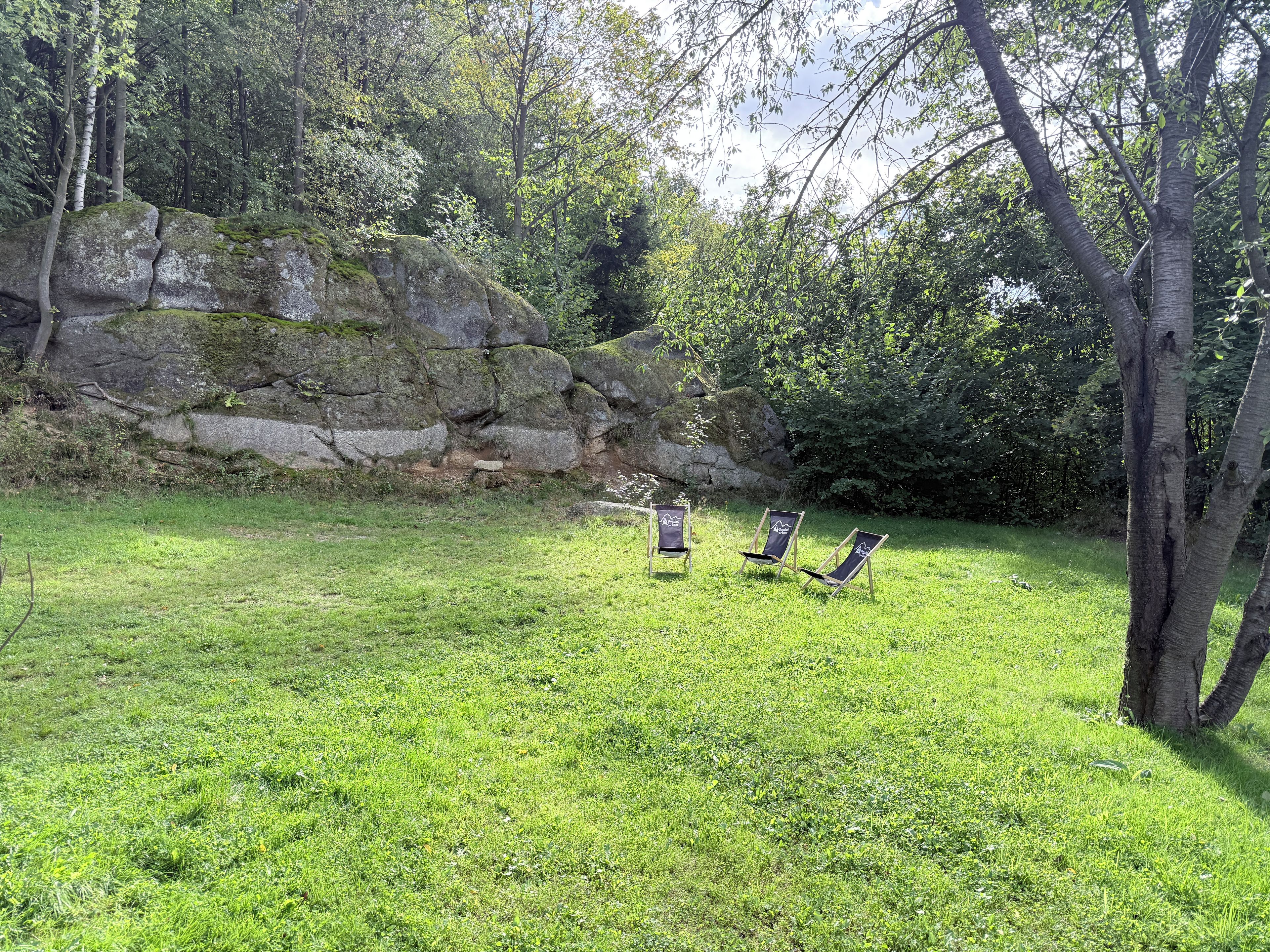 Un espacio al aire libre con césped, tres sillones de descanso y un paisaje rocoso de fondo.