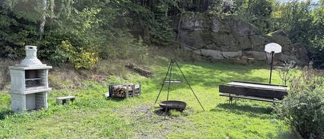 A grassy outdoor area with a stone structure, a swing set, a basketball hoop, and a bench.