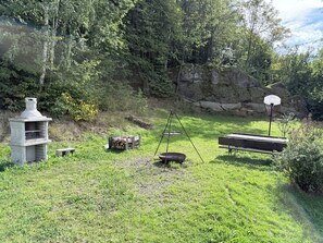 A grassy outdoor area with a stone structure, a swing set, a basketball hoop, and a bench.