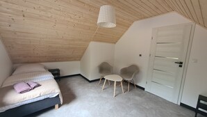 Un dormitorio con techo inclinado, una cama con cabecera, dos sillas, una mesita y una puerta blanca.