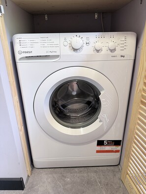 A front view of a white Indesit washing machine with a control panel, a 5kg capacity label, and a 5-year free registration guarantee sticker.