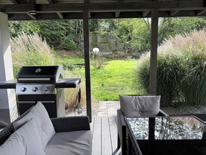 Une terrasse extérieure avec un barbecue, des meubles en osier et une vue sur une pelouse.