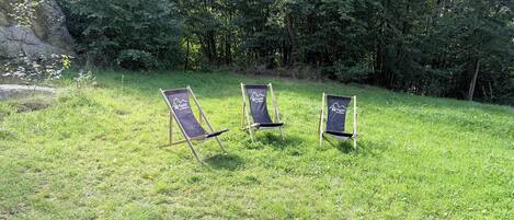Three outdoor lounge chairs with a logo, set on a grassy area with trees in the background.