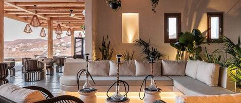 A spacious lounge area with a large sofa, multiple seating options, and hanging plants.