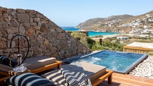 Zona d'una piscina al terrat amb parets de pedra, gandules i vista al mar i a les colines.