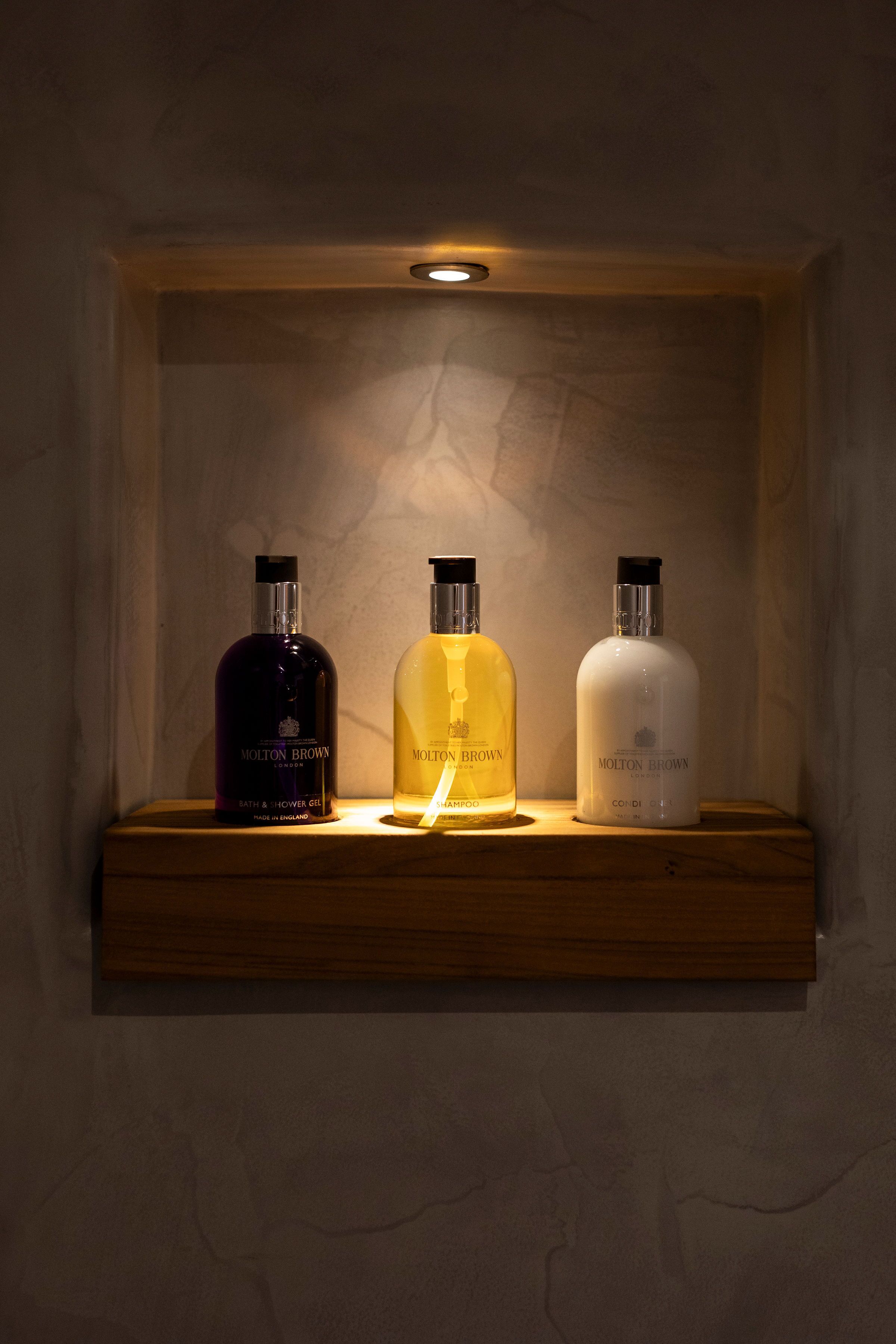 Three bottles of Molton Brown bath and shower gel on a wooden shelf.