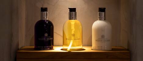 Three bottles of Molton Brown bath and shower gel on a wooden shelf.