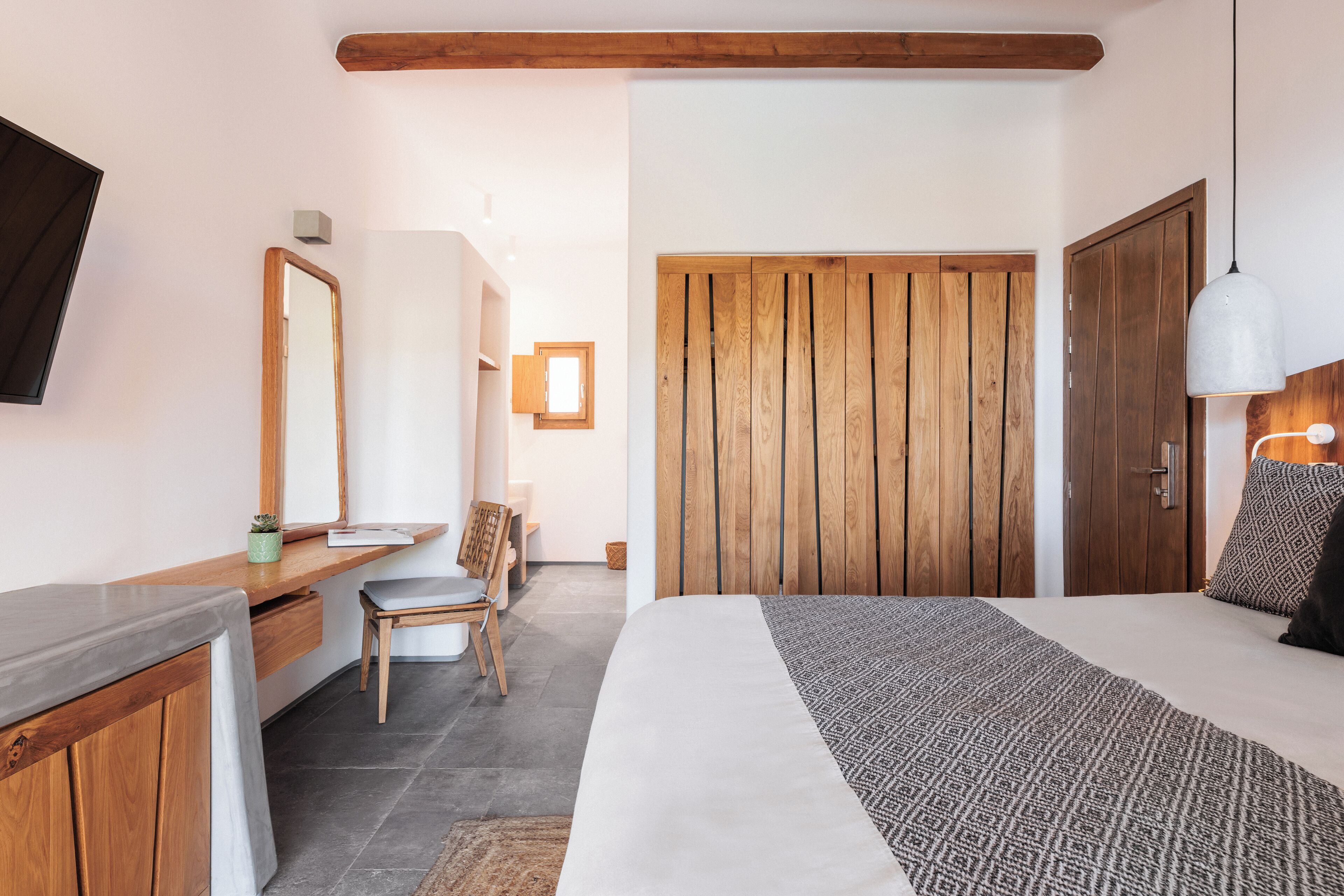 Un dormitorio con cama, armario de madera, mesita de noche, silla y televisor montado en la pared.