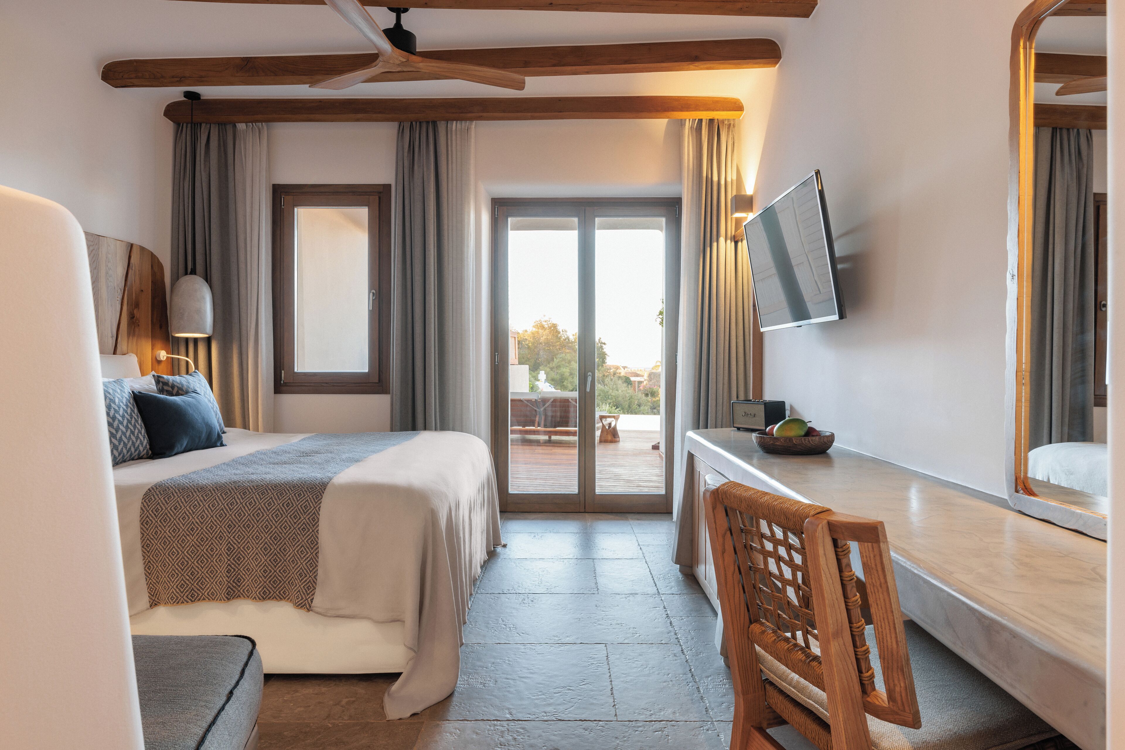 A hotel room with a bed, a desk, a chair, a television, and a sliding glass door leading to an outdoor area.