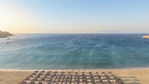 Una platja amb aigua blava cristal·lina, una filera de sombrerets i una muntanya al capdamunt.