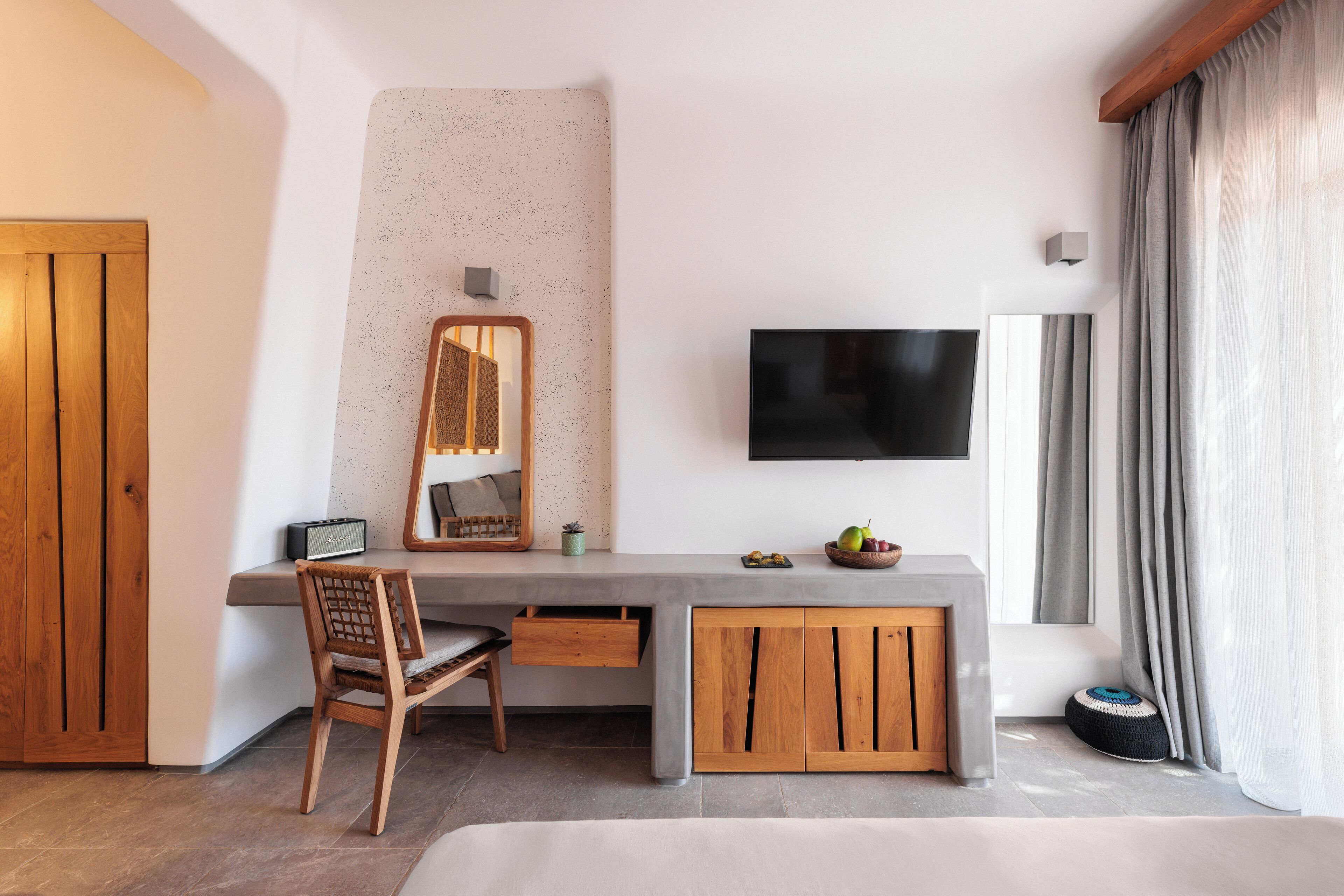 A modern bedroom with a wooden desk, a flat-screen TV, a large mirror, and a bed.