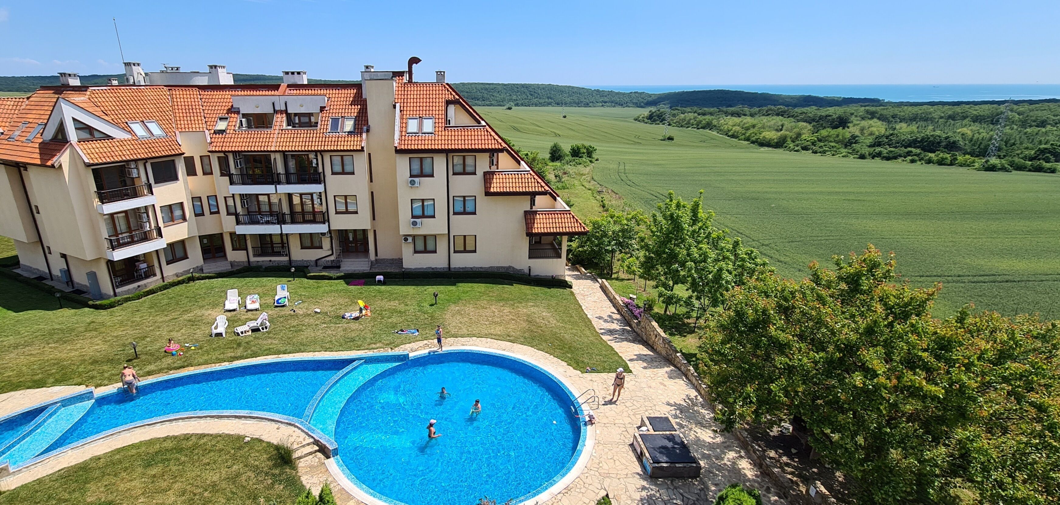 Un edificio de varios pisos con piscina, rodeado de un césped cuidado y vistas a un campo verde.