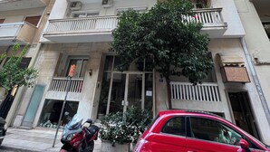 A multi-story building with balconies, a parked motorcycle, and a red car on the street. - A cosy studio in the heart of the upscale neighborhood of Kolonaki (Athens)