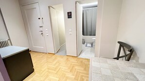 A room with a herringbone wood floor, a white door, a bathroom visible through an open door, and a small table with a chair. - A cosy studio in the heart of the upscale neighborhood of Kolonaki (Athens)